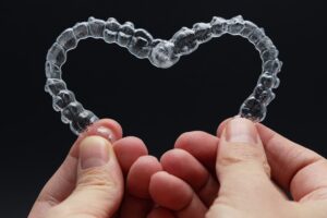 Manos formando un corazón con férulas transparentes de ortodoncia invisible | Ortodoncia Invisible | Dentista Madrid Río | Estética Dental